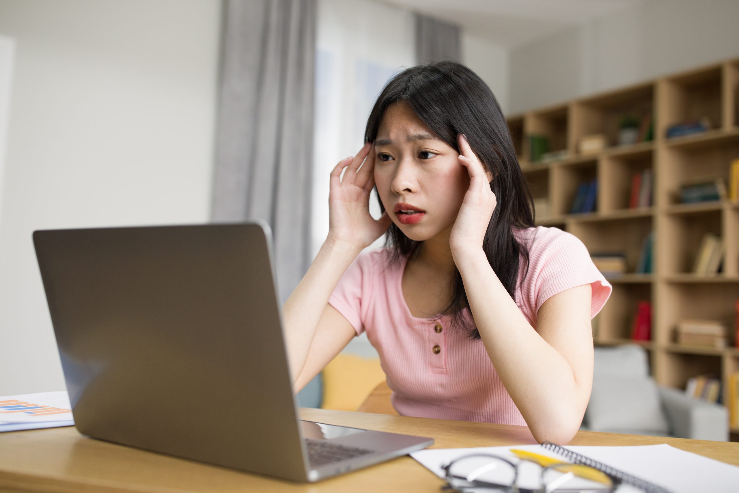 Sad tired asian lady with laptop suffering from headache, pressing hands to temples, sitting at desk