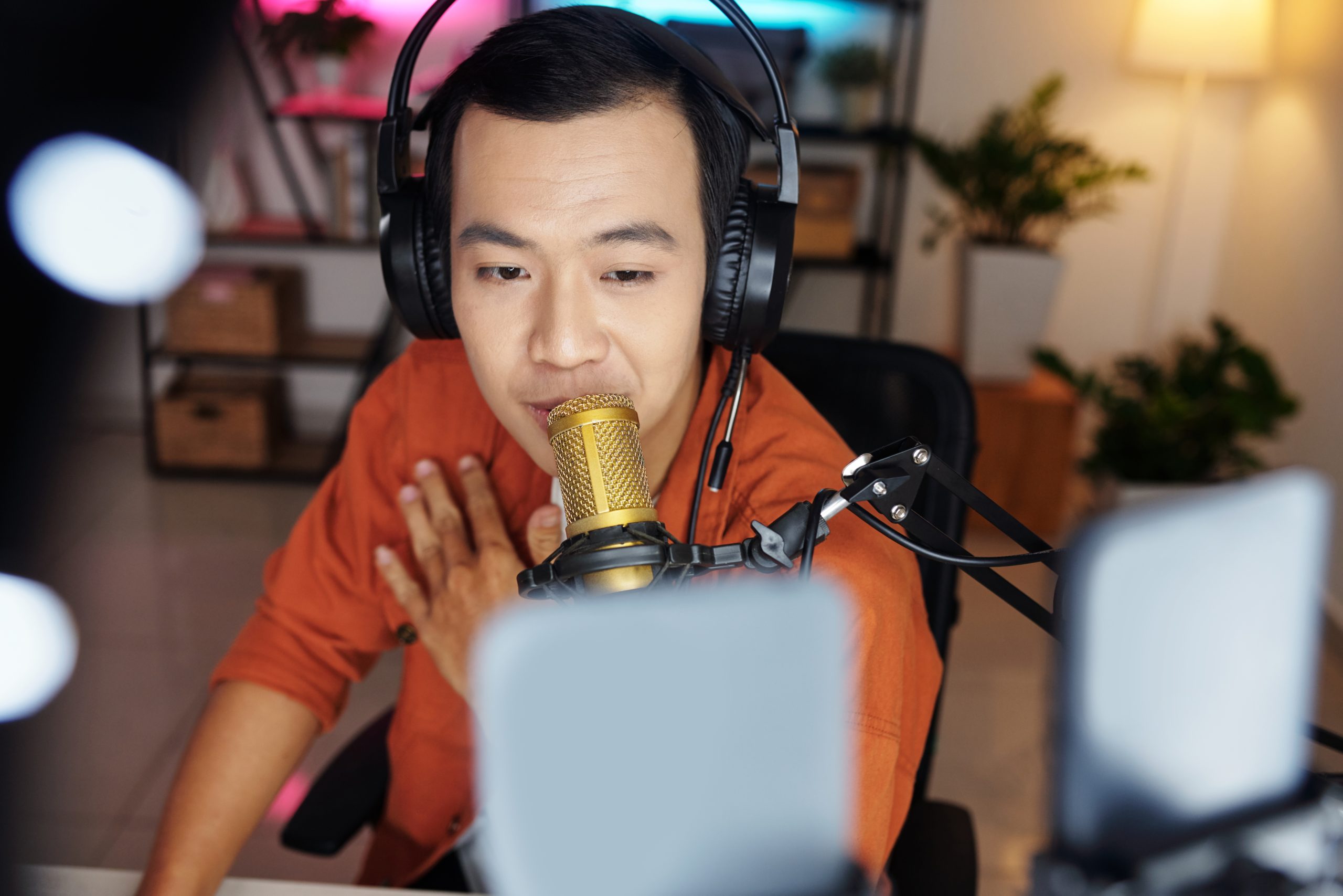 A man is sitting in front of his laptop with a microphone. He is making content for a video blog.