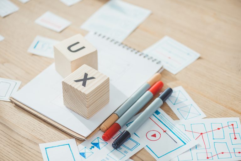 Selective focus of letters ux on cubes with website app development sketches on wooden table