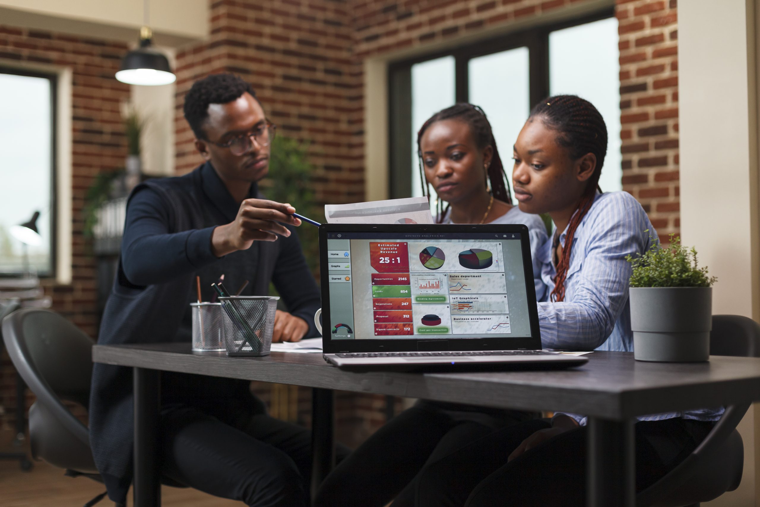 Agency office workers cooperating regarding startup project marketing expenses while in modern meeting room. African american business people discussing financial strategy while in workspace.