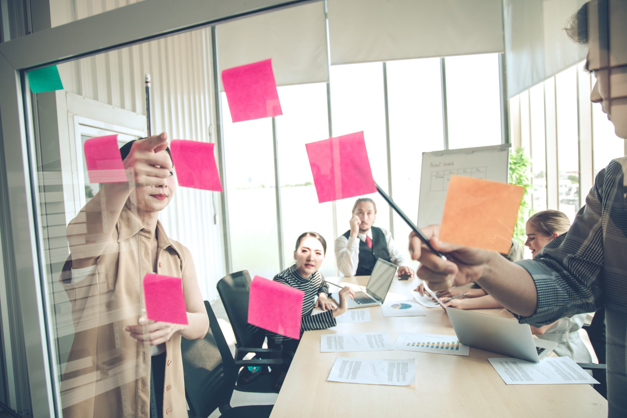 People are in a meeting room and are smiling. There are sticky notes being pointed to.