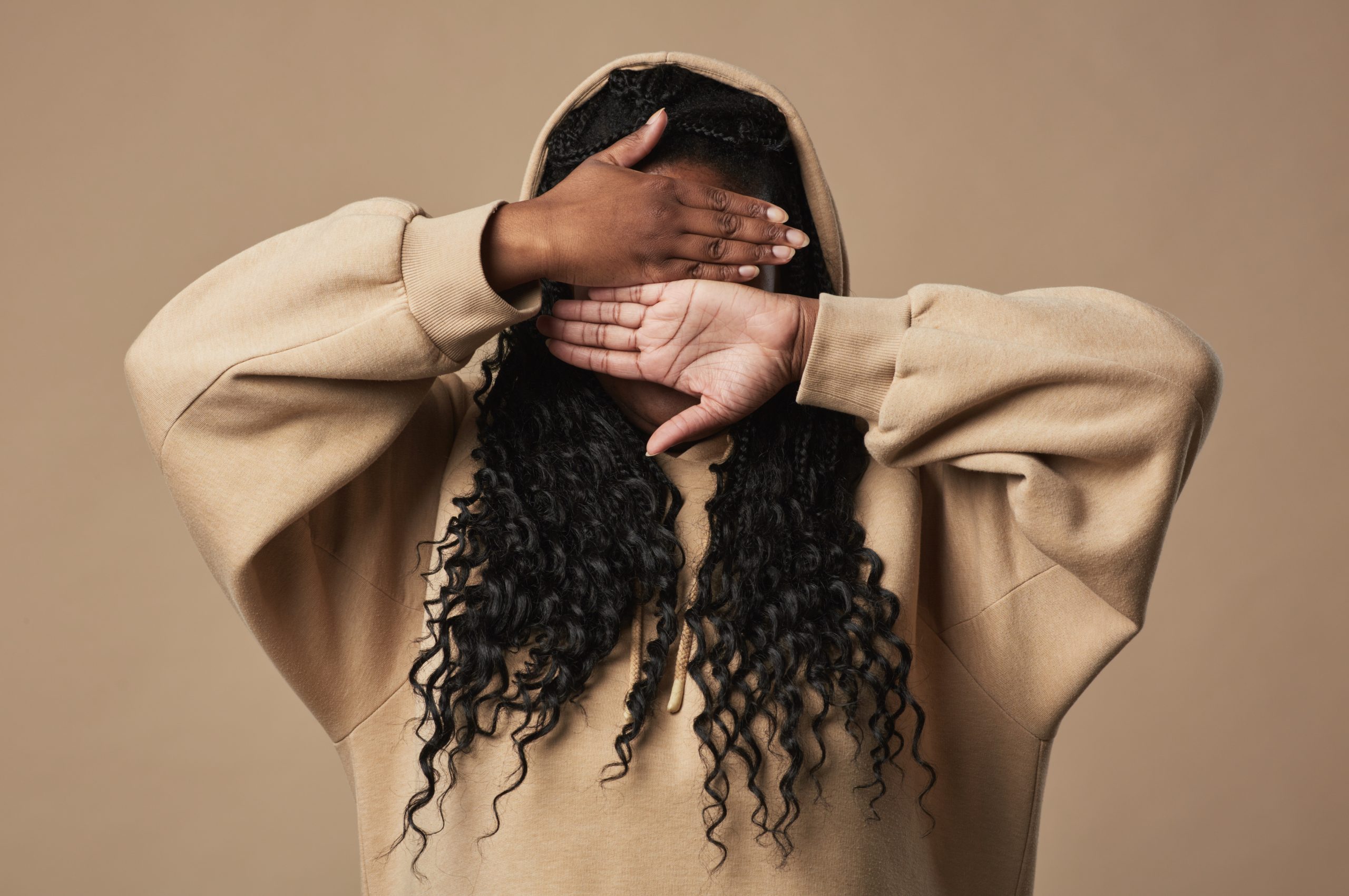 A woman wearing a hoodie. She is covering her face with both of her hands.