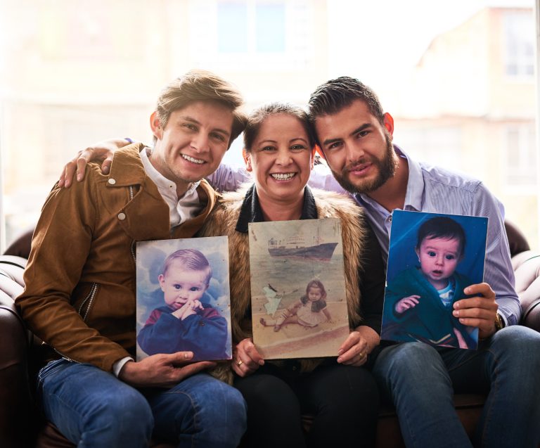 Shot of a mother and sons holding old photographs of themselves as children at home.