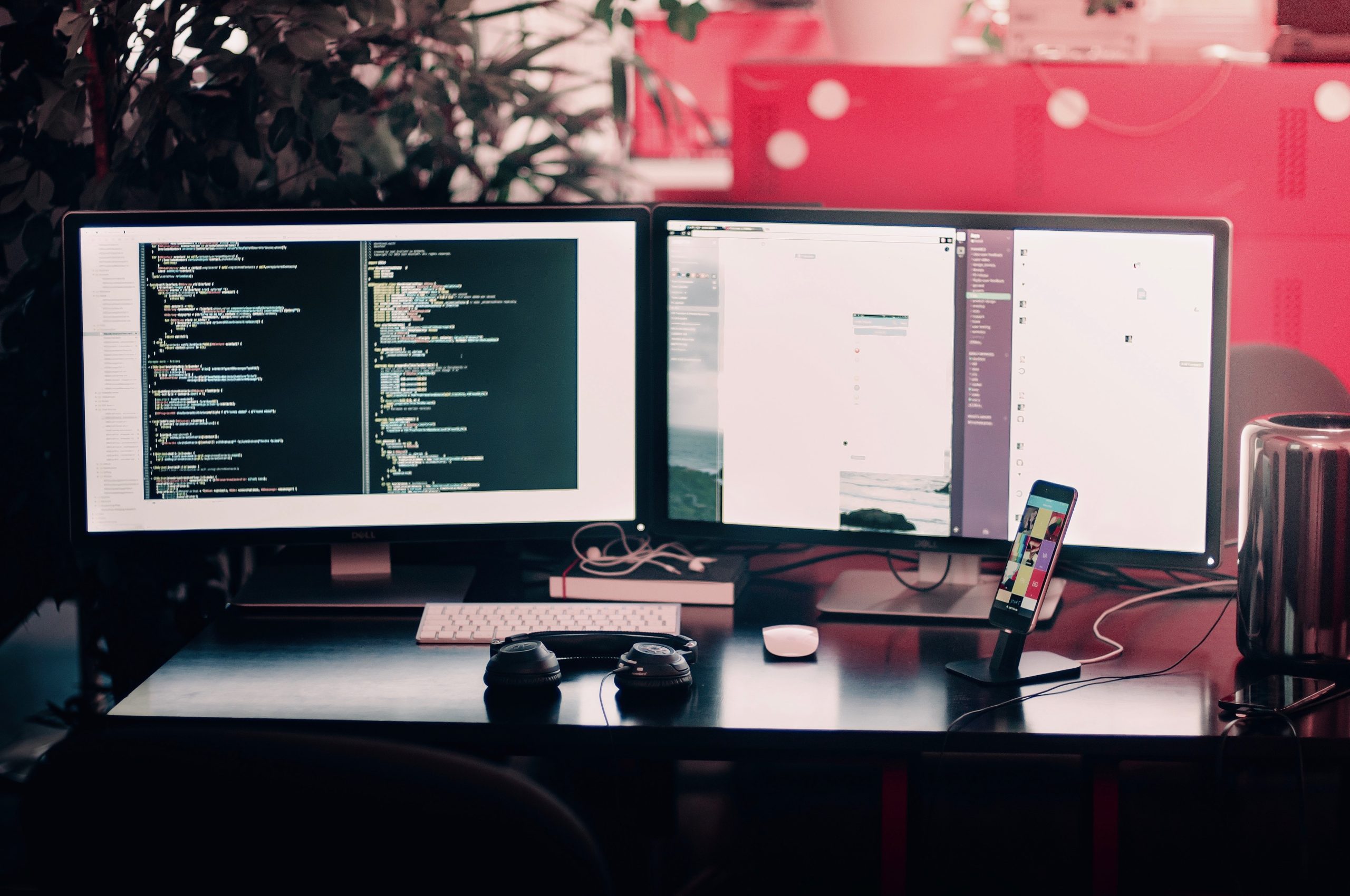 Two black computer monitors on a black desk with headphones and two phones.